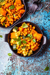 Baked sweet potato, zucchini and chickpeas in cast iron pan, blue background, top view. Baked vegetables. Healthy food concept.