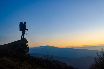 Hiker with backpack on the mountain top enjoys the sunset.