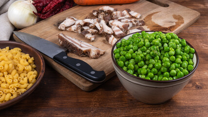 Ingredients for making pasta with peas and pancetta on a rustic wooden table - pancetta, bacon, peas, onions, carrots, chifferini