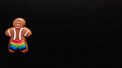 Lgbt pride. Black conceptual background. Diversity tolerance. Individuality freedom. Happy African gay gingerbread man in rainbow shorts on dark wooden texture copy space.