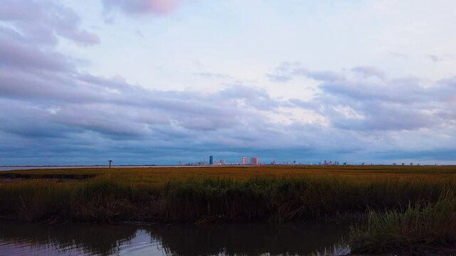 HD MOTIONLAPSE Straight pan from left to center and hold Atlantic City skyline in distance over waterway with mostly cloudy sky day to night with clouds turning pink, purple and blue
