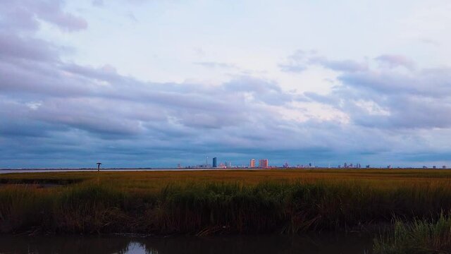 HD MOTIONLAPSE Zoom in from left to center and hold Atlantic City skyline in distance over waterway with mostly cloudy sky day to night with clouds turning pink, purple and blue