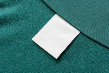 Blank white laundry care clothes label on green fabric texture background