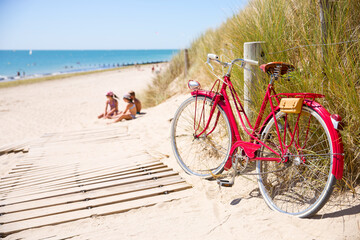 Enfant sur la plage jouant dans le sable à côté d'un vieux vélo rouge abandonné par un vacancier.