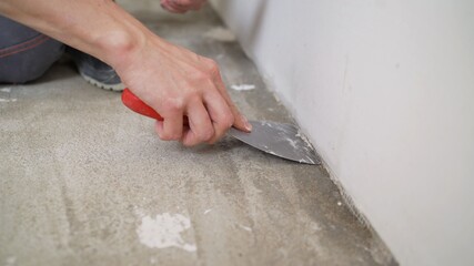 A worker cleans the floor with a spatula, repairs. Close-up of a hand and a spatula. A worker cleans the floor with a spatula.