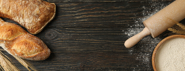 Fresh bread, flour, spikelets and rolling pin on wooden background
