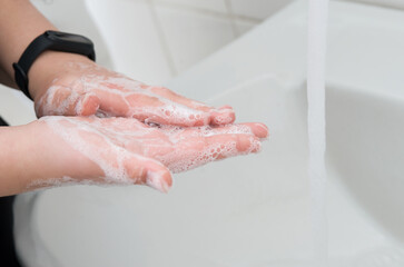 Young adult washing hands with soap in bathroom.