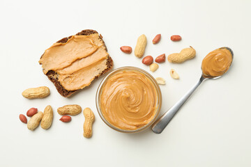 Jar, spoon and sandwich with peanut butter on white background