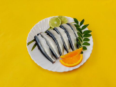 Cleaned and ready to cook fresh indian sardine decorated with curry leaves,lemon slice and tomato slice .Isolated on yellow background.