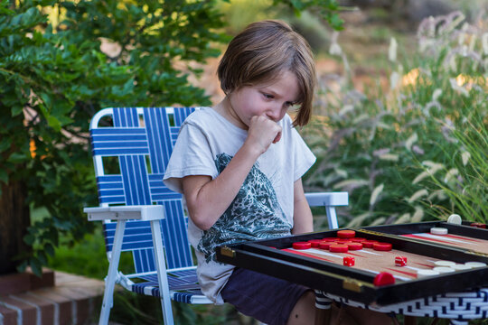 A young boy playing backgammon outdoors in a garden. 
