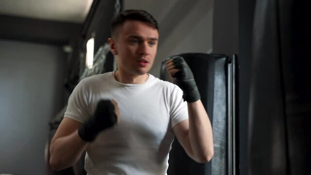Strong athlete man workingout and training with a punching bag. Male boxer with wrapped hands in the gym.