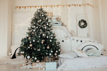 Christmas tree  decorated with white balls and garlands. Under tree stand gifts. A white car near Christmas tree. Bright home interior.