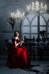 Bloodthirsty female vampire in red dress. Medieval interior