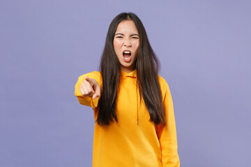 Angry irritated young brunette asian woman wearing casual basic yellow hoodie standing pointing index finger on camera screaming swearing isolated on pastel violet colour background studio portrait.