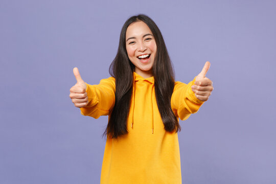 Cheerful Laughing Attractive Young Brunette Asian Woman 20s Wearing Basic Casual Yellow Hoodie Standing Showing Thumbs Up Looking Camera Isolated On Pastel Violet Colour Background Studio Portrait.