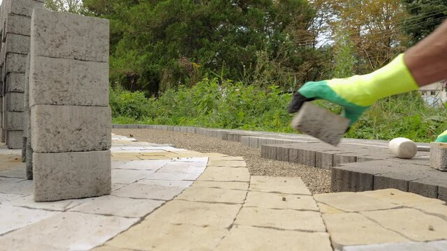 Construction worker laying pavement rocks on the street Builder makes a walkway with stone bricks or concrete pavers.