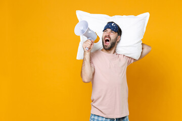 Angry young bearded man 20s in pajamas home wear sleep mask hold pillow screaming in megaphone...