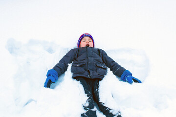 Fototapeta na wymiar The child is lying on the snow in the pose of a snow angel. Boy on ice in a snow field