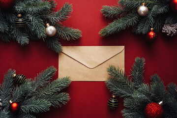 Fototapeta na wymiar Fir tree branches, Xmas empty envelope on red background. Flat lay, top view, copy space. Concept of letter to Santa Claus