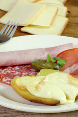 fromage à raclette fondu sur une pomme de terre et charcuterie dans une assiette