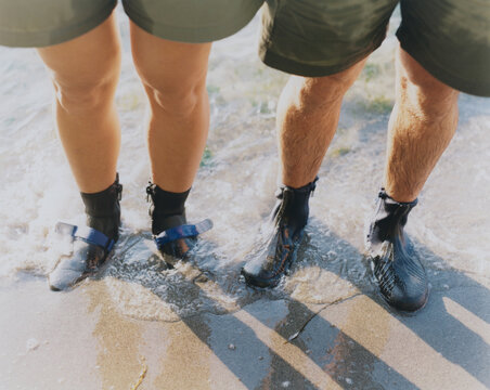Man and woman wearing waterproof booties, standing in surf