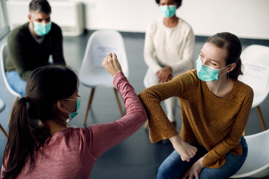 Two women with face masks elbow bumping during group therapy session.