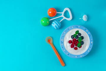bowl with yogurt, for a child, with blueberries and raspberies, on a blue background, horizontal