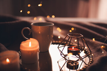 Cup of hot tea with burning candles on tray in bed over Christmas lights close up. Night time...