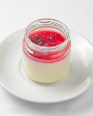 Panna cotta in a glass on white plate with berry sauce. Traditional Italian dessert isolated on white.