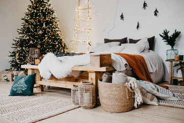 Comfortable bedroom in bohemian interior style with textile sheet on bed, christmas tree on...