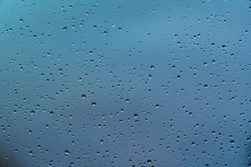 Water drops on window glass after rain. Macro of raindrops as abstract background with shallow depth of field. Concepts of rainy weather in autumn or winter season, cold temperatures and melancholy.