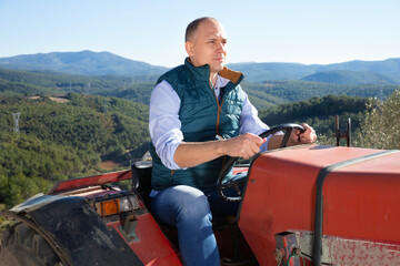 Confident cheerful smiling glad male owner of vineyard driving tractor outdoors in sunny day