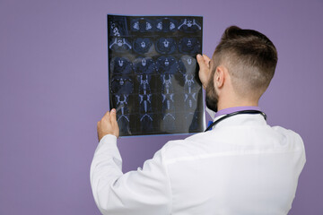 Back rear view of young bearded doctor man in medical gown stethoscope hold x-ray brain by...