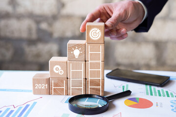 Businessman hand arranging wood block stacking with 2021 new year goal achievement icon. Business...