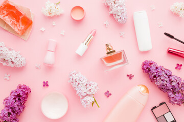 Various decorative makeup cosmetics and fresh colorful lilac flower blossoms on pink pastel table background. Different beauty essentials for women. Closeup. Top down view. Beauty pattern.
