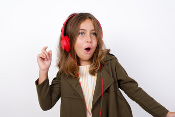 Beautiful little girl standing against white background, , dancing and listening music with headphones.