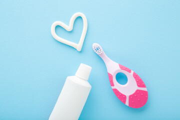 White heart shape, tube of toothpaste, pink toothbrush on light blue table background. Pastel color. Babies teeth hygiene. Closeup. Top down view.