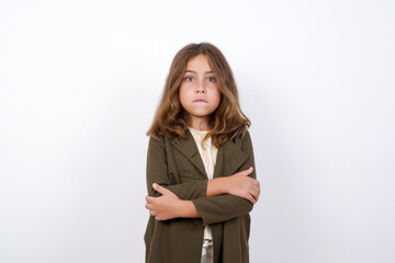 Beautiful little girl standing against white background,  bitting his mouth and looking worried and scared crossing arms, worry and doubt.
