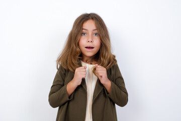 Portrait of desperate and shocked Beautiful little girl standing against white background, looking panic, holding hands near face, with mouth wide open.