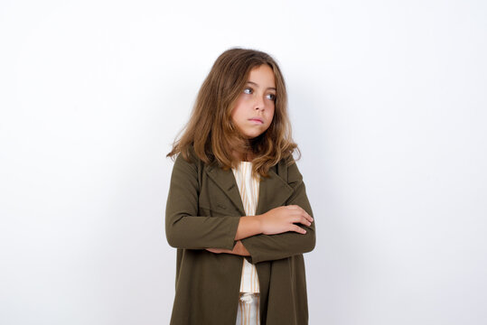 Displeased Beautiful little girl standing against white background, with bad attitude, arms crossed looking sideways. Negative human emotion facial expression feelings.