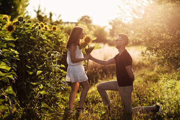 Beautiful couple having fun in sunflowers field. A man and a woman in love walk in a field with sunflowers, a man hugs a woman. selective focus