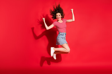 Full body photo of young attractive girl wear mini skirt happy smile jump fists hands x-mas isolated over red color background