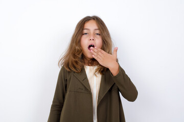 Sleepy Beautiful little girl standing against white background, yawning with messy hair, feeling tired after sleepless night, yawning, covering mouth with palm.