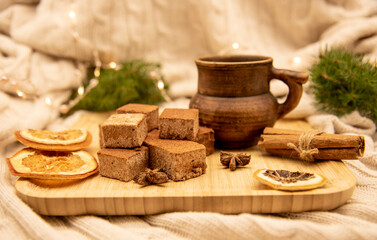 A clay mug with a drink and various Goodies are on a wooden tray, standing on a knitted blanket .
