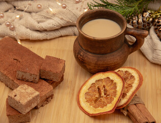 A clay mug with a drink and various Goodies are on a wooden tray, standing on a knitted blanket .