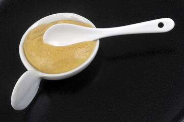 Ramequin de moutarde avec une cuillère en gros plan sur fond noir