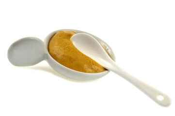 Ramequin de moutarde avec une cuillère en gros plan sur fond blanc