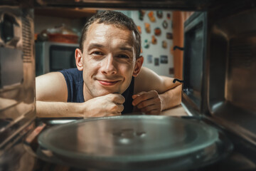 Dark-haired man has opened an empty microwave oven and is looking at it smiling, a photo from...