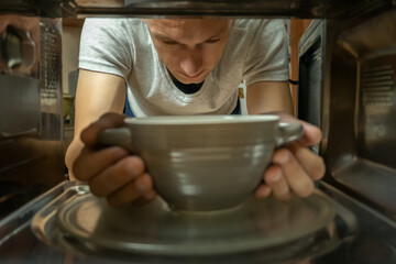 Men's gray hands get a bowl out of the microwave is a close-up photo from the inside.