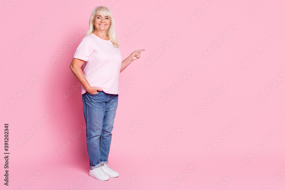 Poster Photo portrait of elderly woman pointing finger at blank space isolated on pastel pink colored background